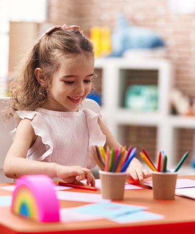 Adorable caucasian girl sitting on table drawing on paper at classroom